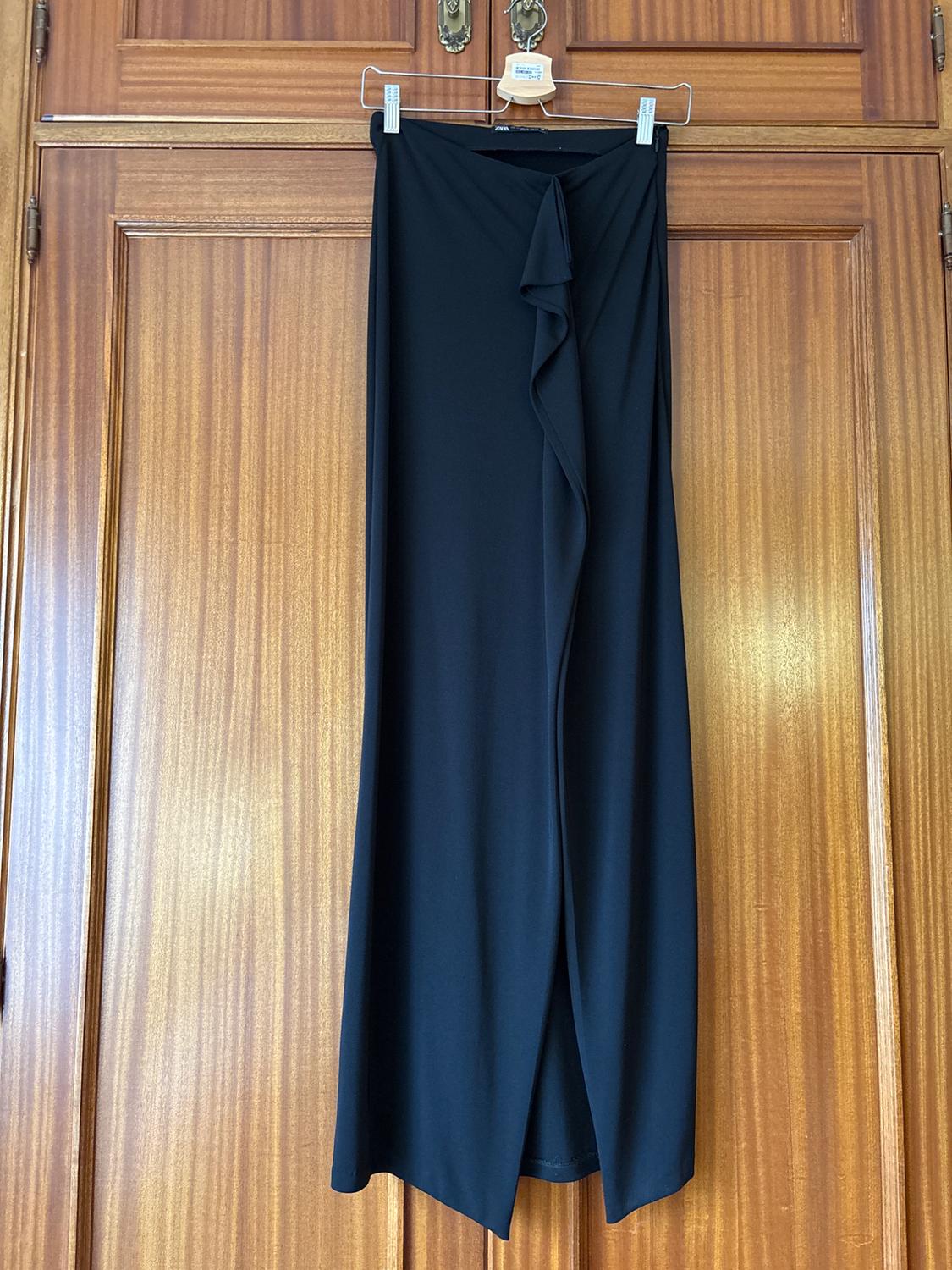 Long black skirt with a frill detail on the front, hanging on a hanger over a wooden door.