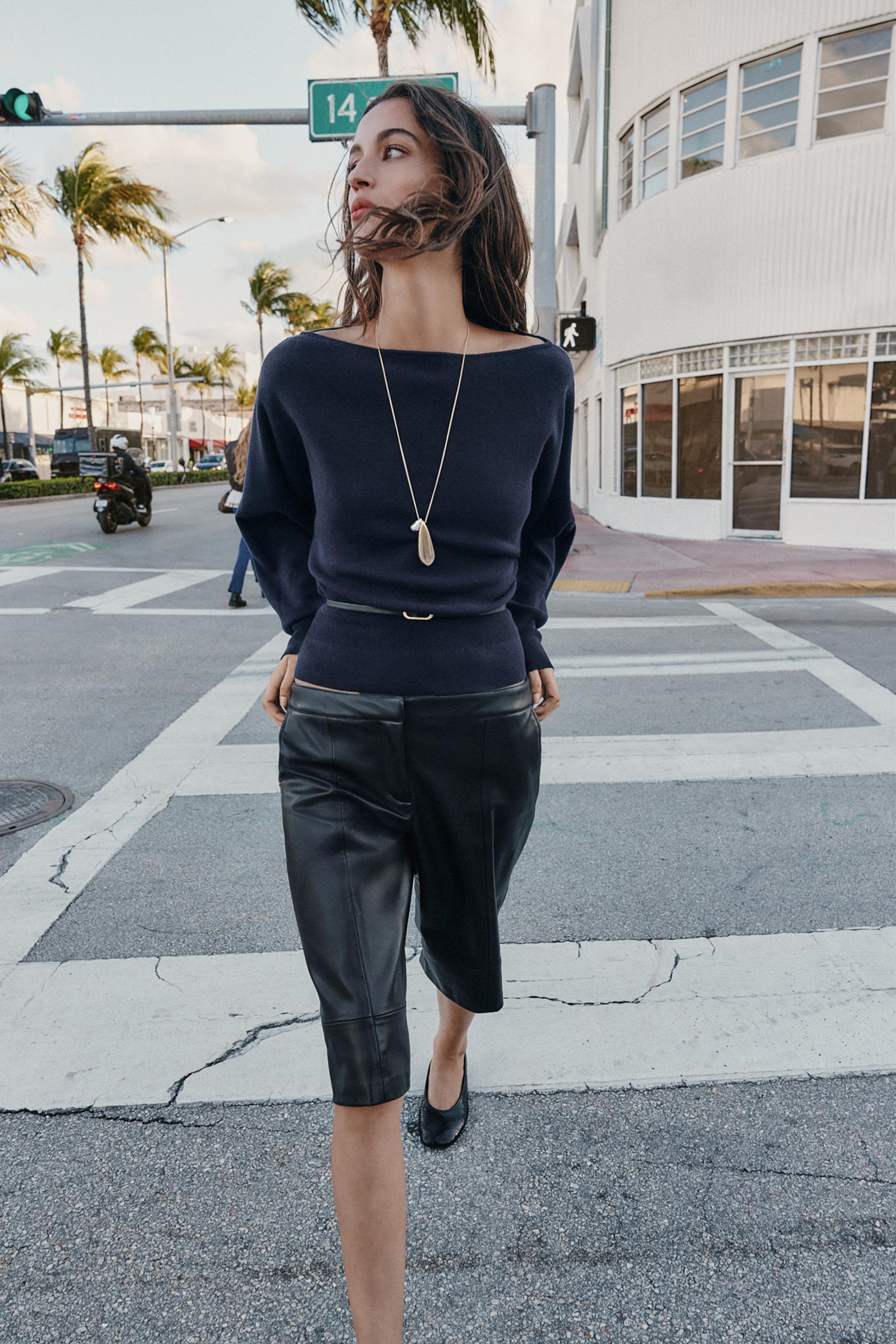 Navy boat neck sweater set with a thin belt, paired with black shorts and flat shoes.