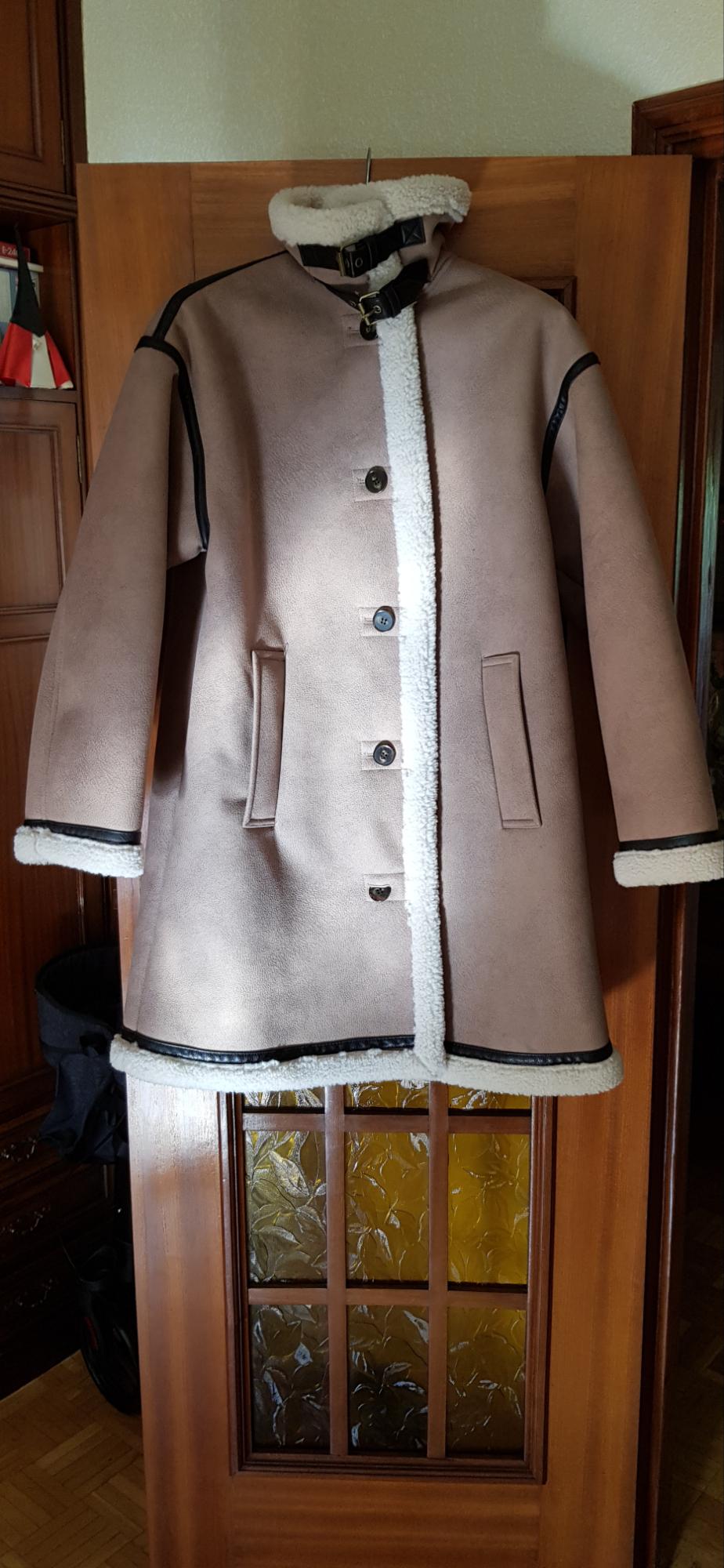 Brown coat with white lining and black details hanging on a wooden door. Front buttons and side pockets visible.