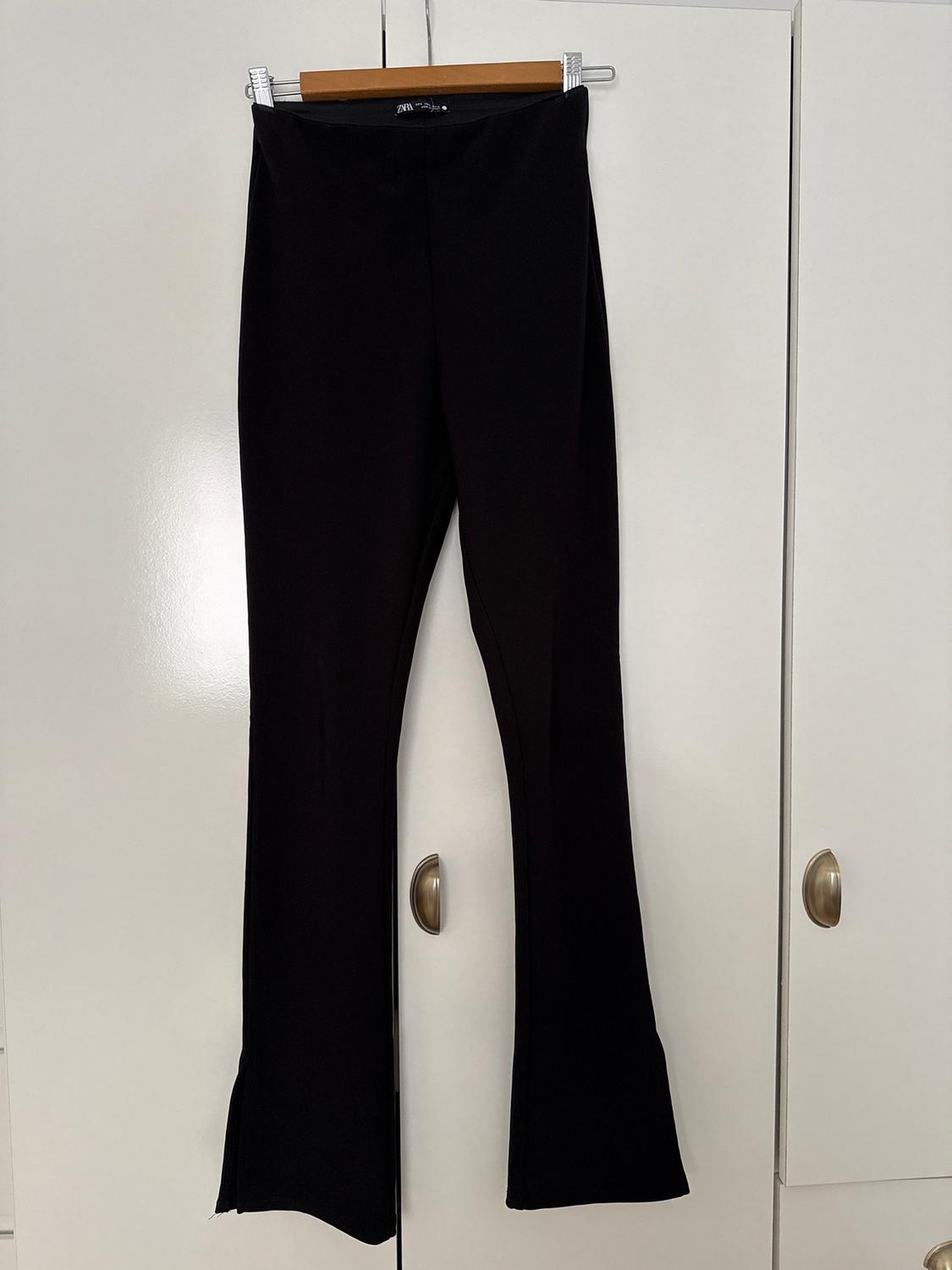Black flared trousers hanging on a wooden hanger in front of a white wardrobe with metal handles.