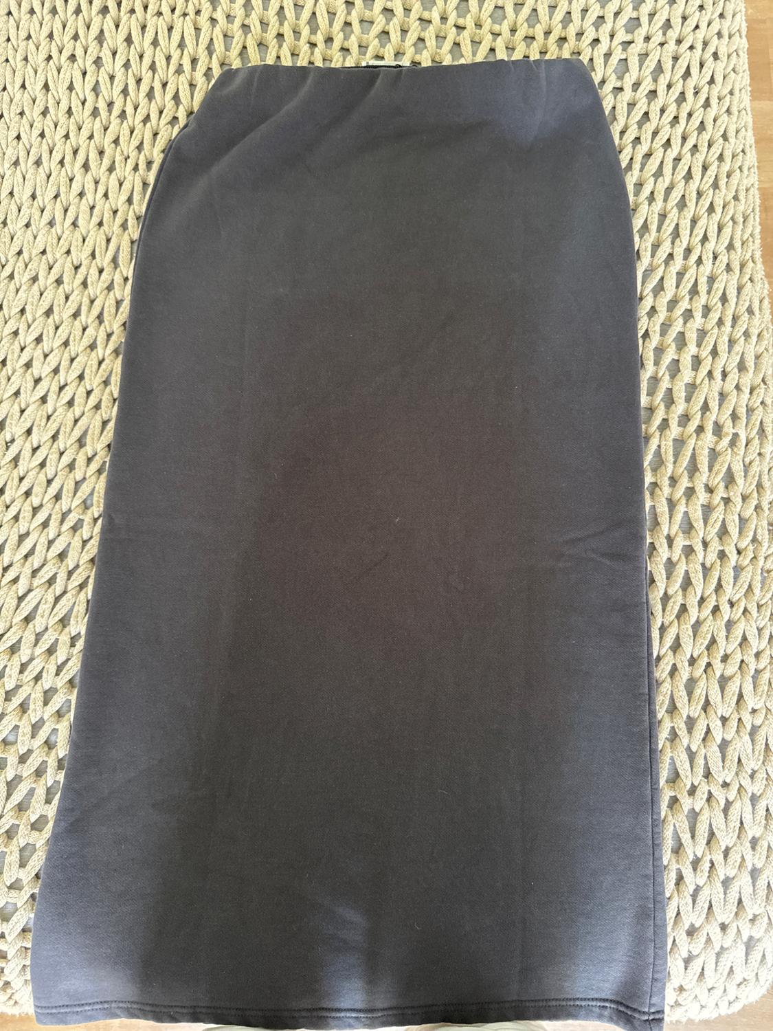 Black skirt on a beige braided fabric surface, viewed from above.