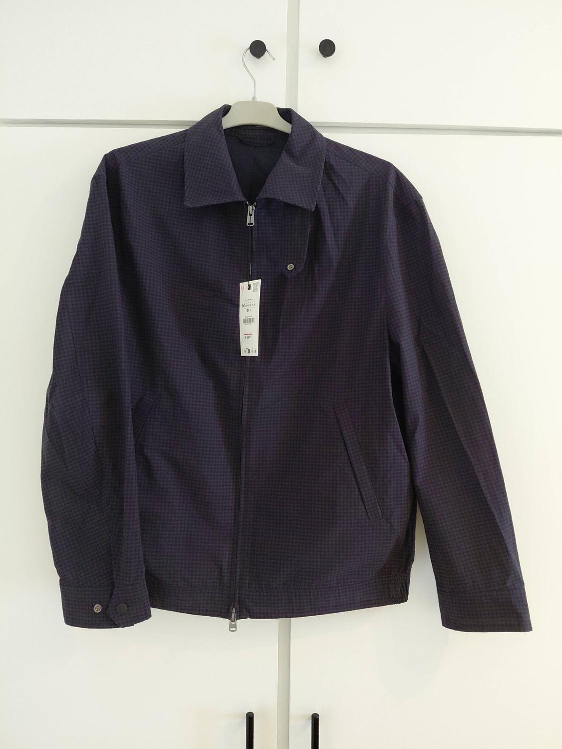 Dark blue jacket with a zip and collar, hanging on a hanger above a white wardrobe with black handles.