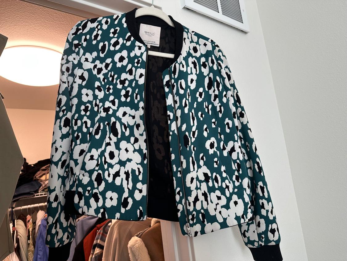 Front view of a black and white floral print jacket on a green background, with a front zipper.