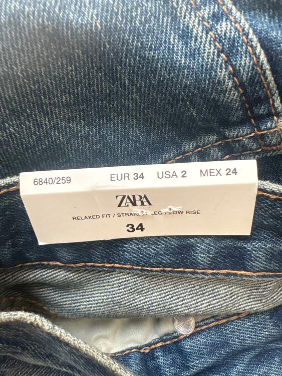 Blue jeans label with orange stitching. Visible text: "ZARA, RELAXED FIT / STRAIGHT LEG / LOW RISE, EUR 34, USA 2, MEX 24, 6840/259".