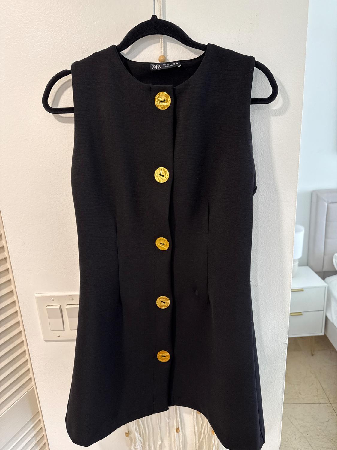 Front view of a black sleeveless dress with large gold buttons.