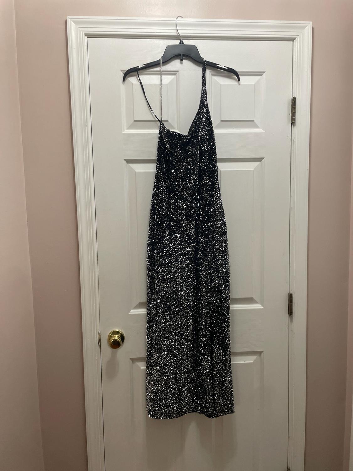 Black sequin maxi dress with spaghetti straps, hanging on a hanger on a white door.