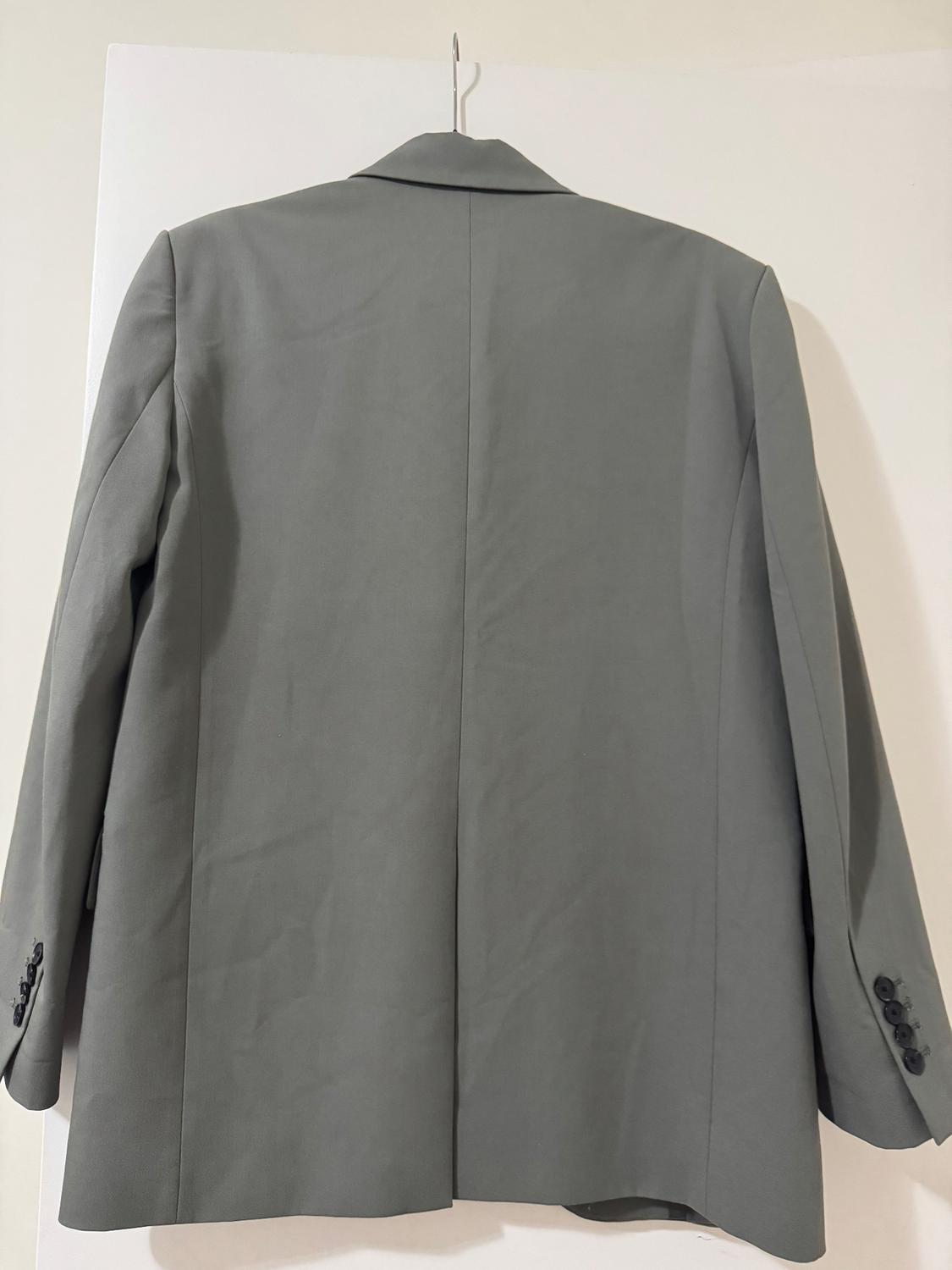 Gray jacket hanging on a hanger, seen from behind. White background, classic design with lapels and buttons on the sleeves.