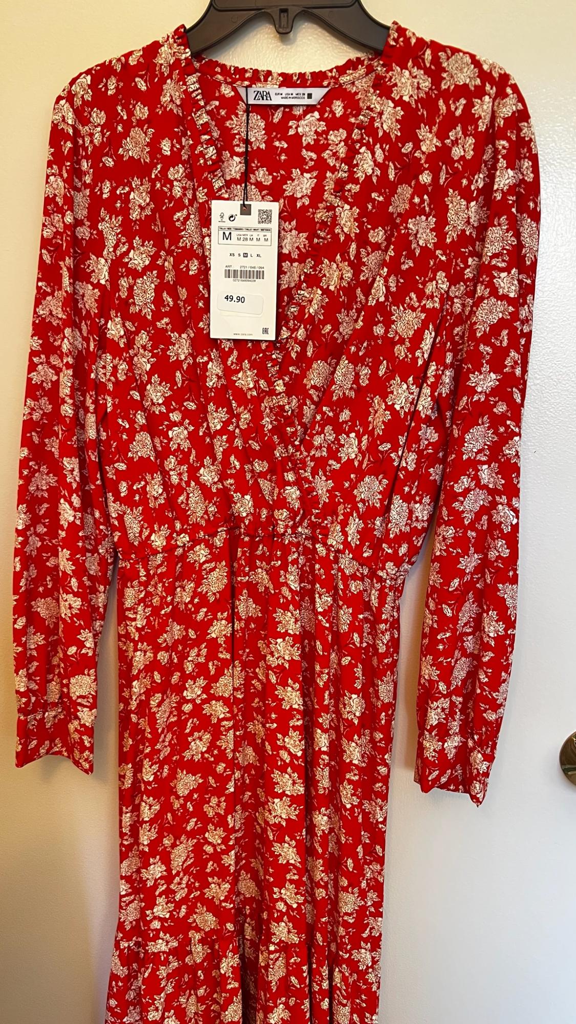 Red dress with a white floral print hanging on a hanger. V-neck and ZARA label with text M and 49.90.