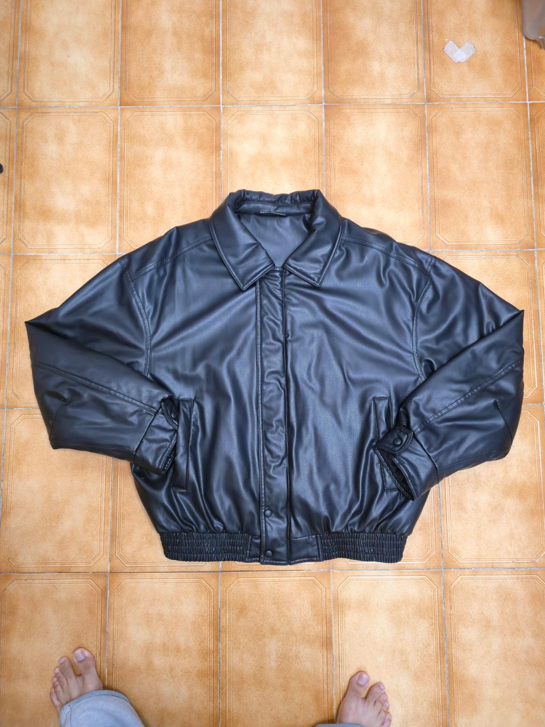 Black jacket spread out on a brown tiled floor. At the bottom edge of the image, a pair of bare feet can be seen.