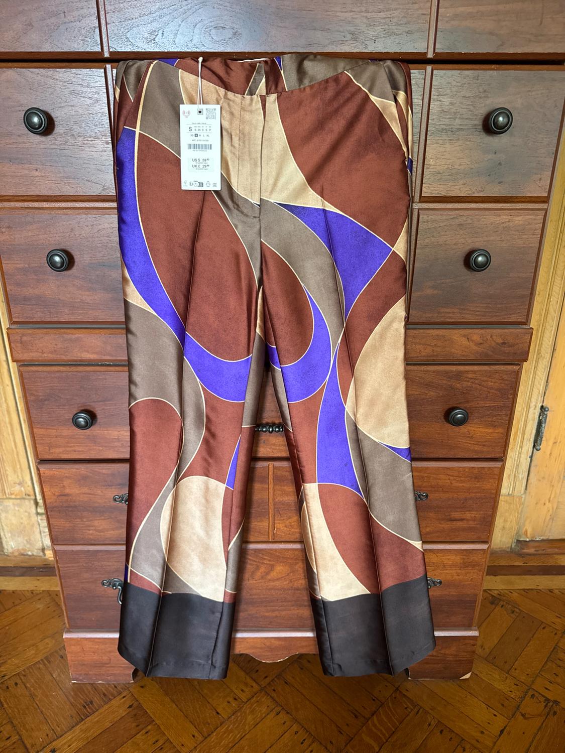 Brown, beige, and purple geometric print pants hanging in front of a wooden dresser. Text: S US$ 59.90 UK£ 29.99.