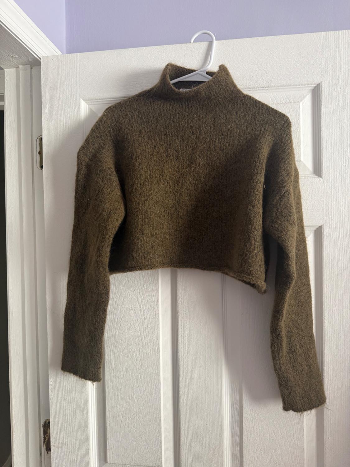 Brown woollen roll-neck jumper with long sleeves, hanging on a white hanger over a white door.