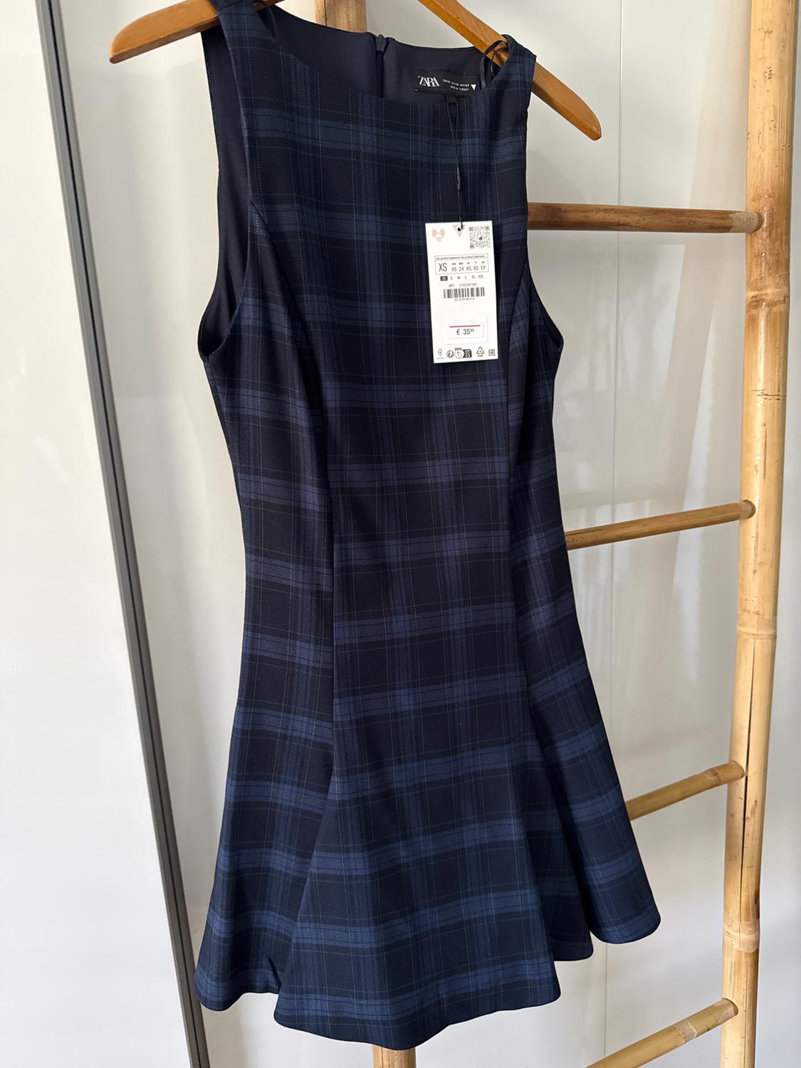 Sleeveless dark blue check dress hanging on a wooden hanger. Visible label with price of £35.95. White background.