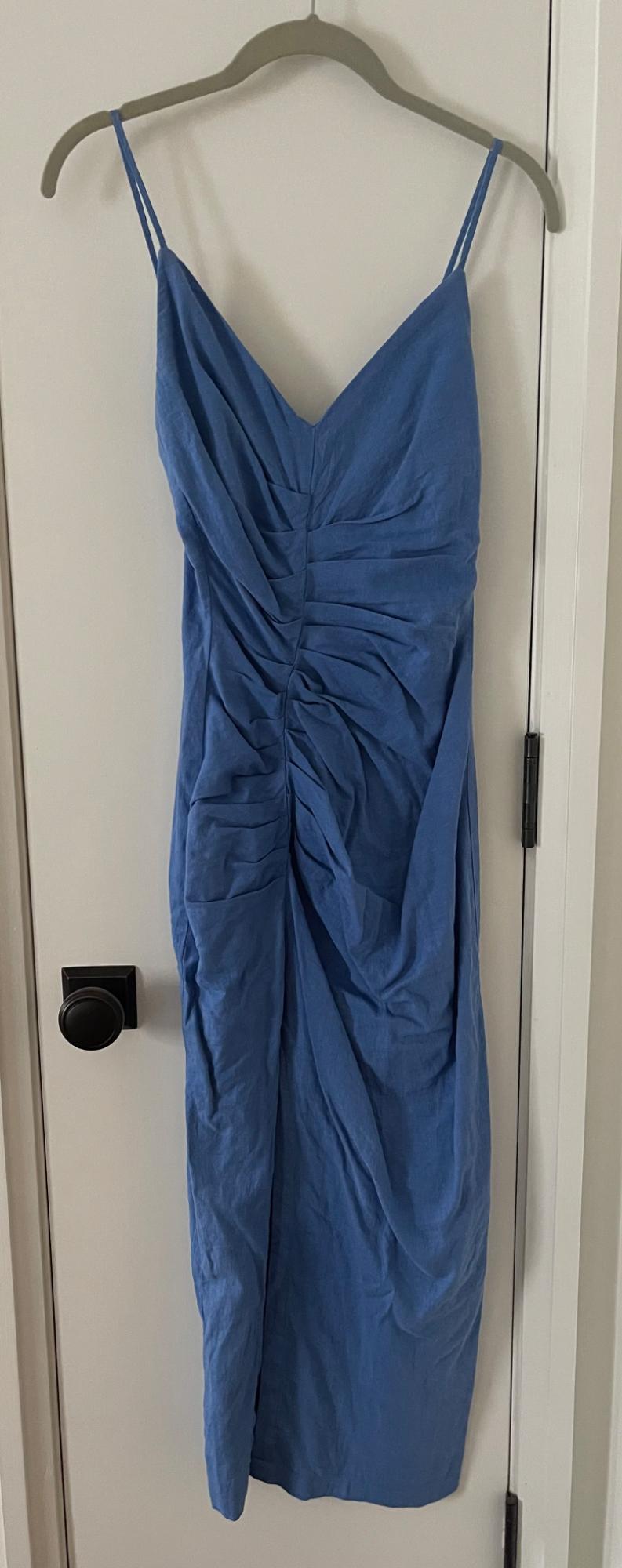 Blue dress with thin straps and a V-neckline with gathered detail, hanging on a hanger on a white door with a black knob.