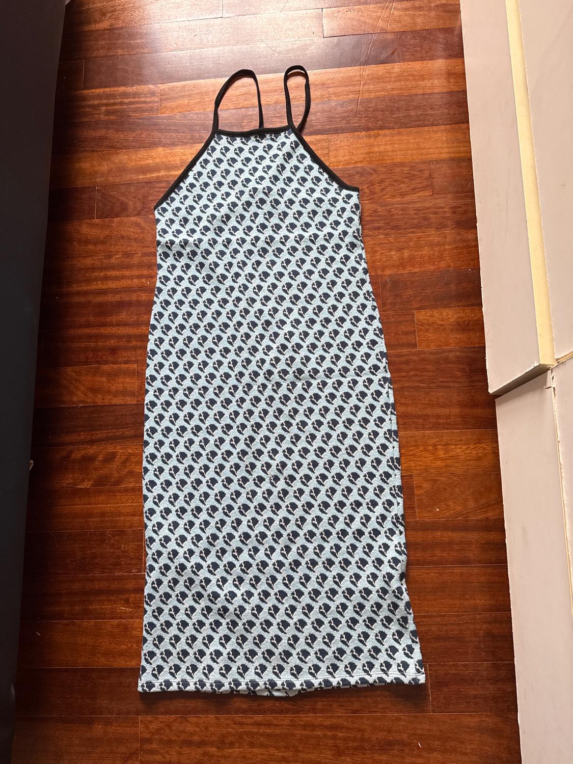 Sleeveless dress with thin straps, black heart print on a white background, on a brown wooden floor.