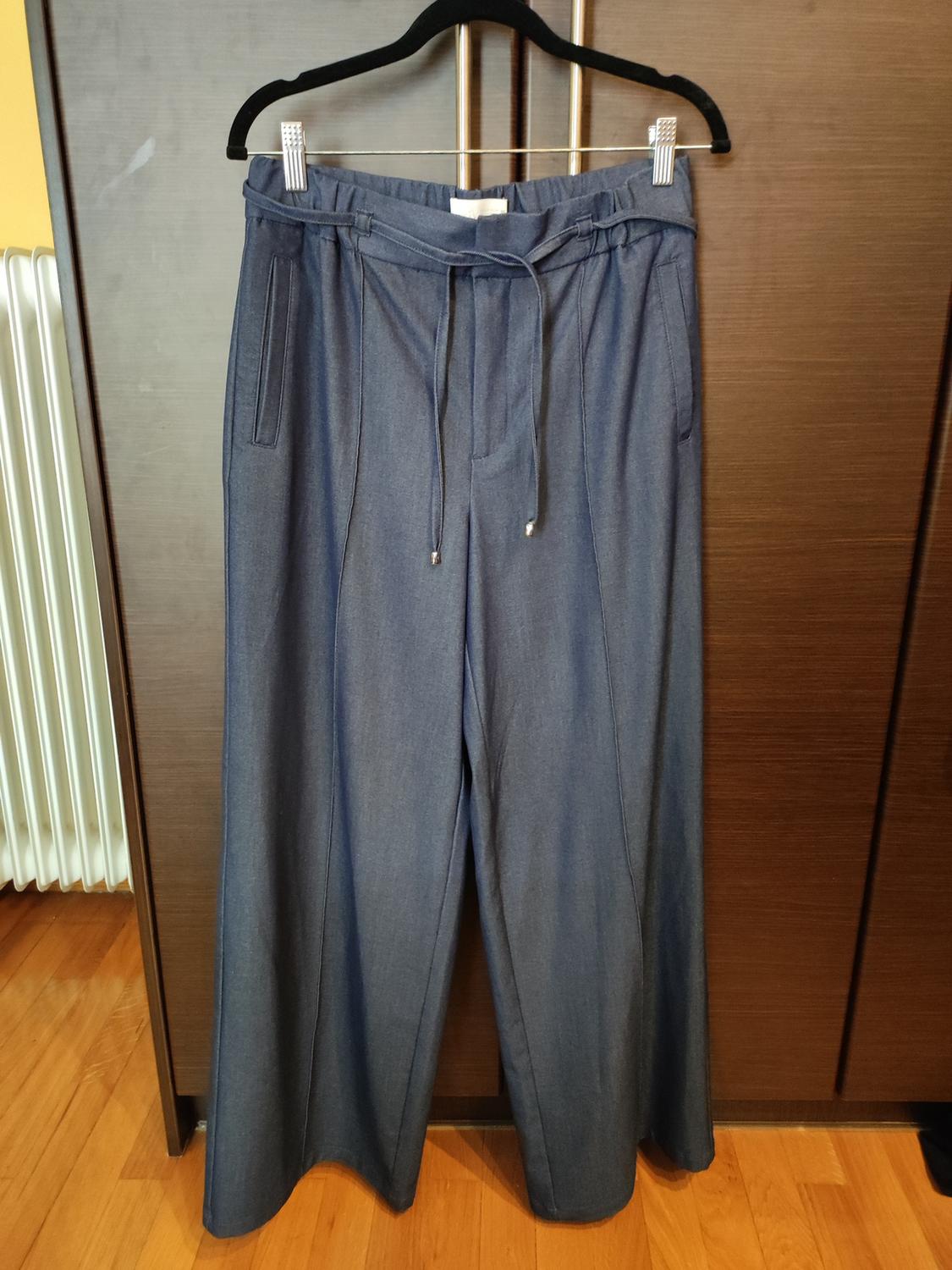 Wide blue denim trousers hanging on a black hanger, with a wooden wardrobe background and parquet flooring.