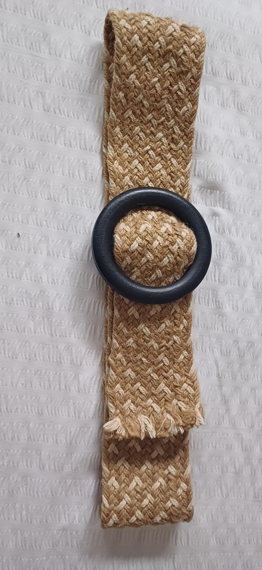 Beige woven belt with a black round buckle on a textured white background.