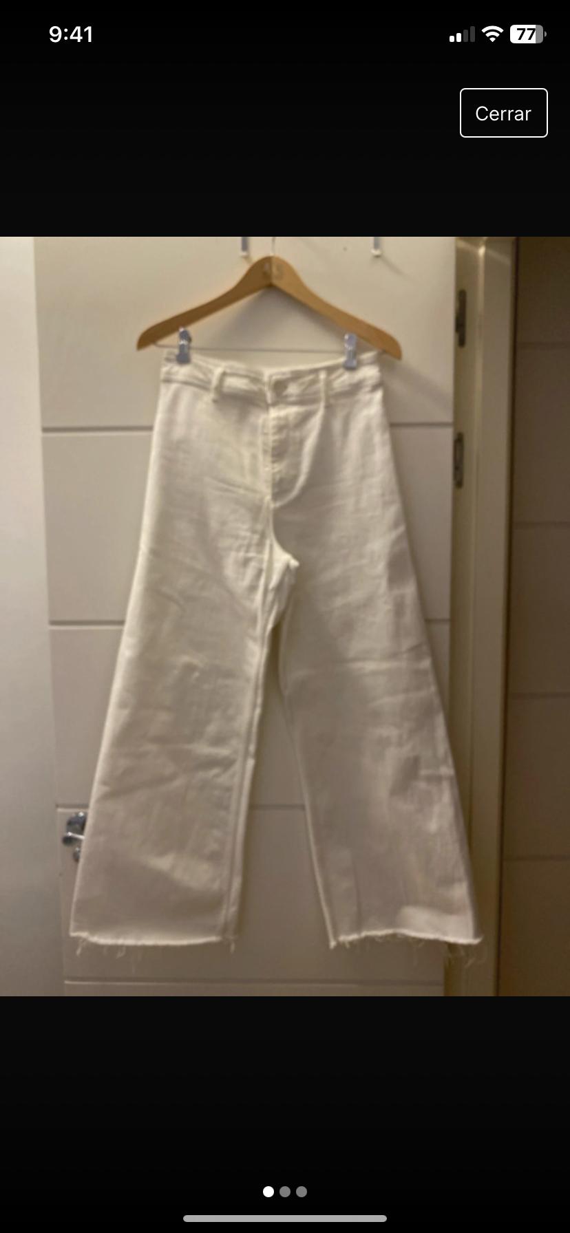 Front view of wide white trousers with a frayed hem hanging on a hanger.