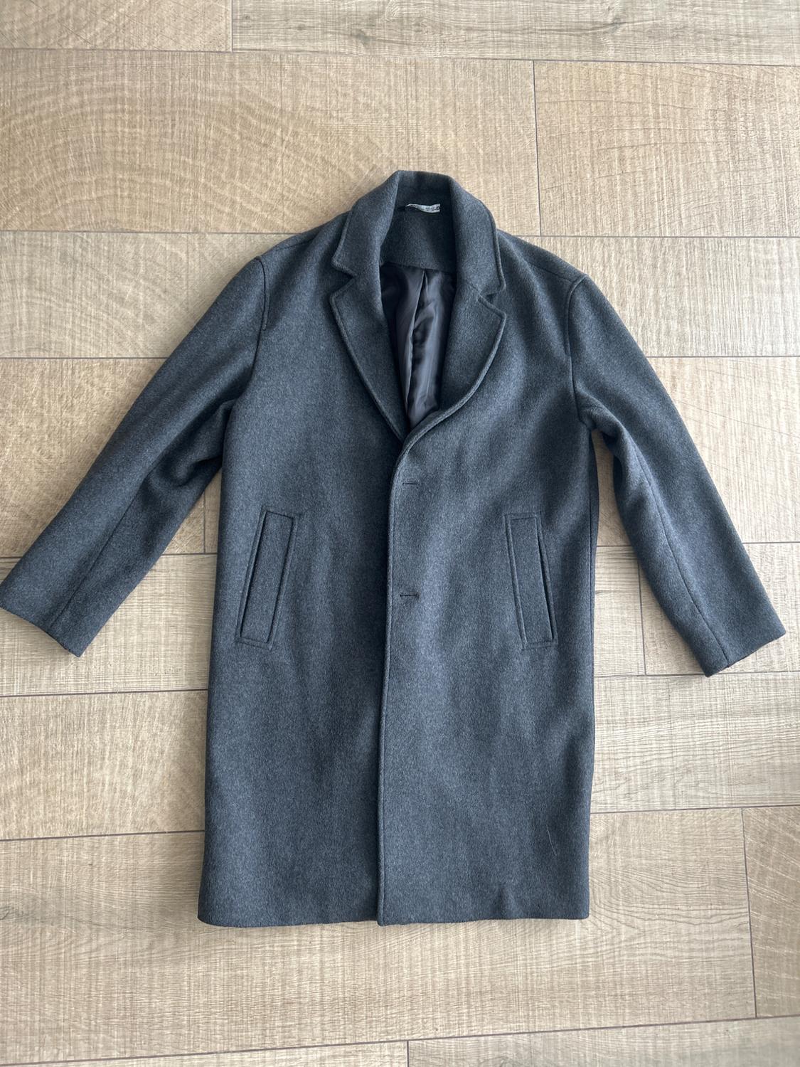 Grey wool coat with lapels and front pockets, spread out on a light wooden floor.
