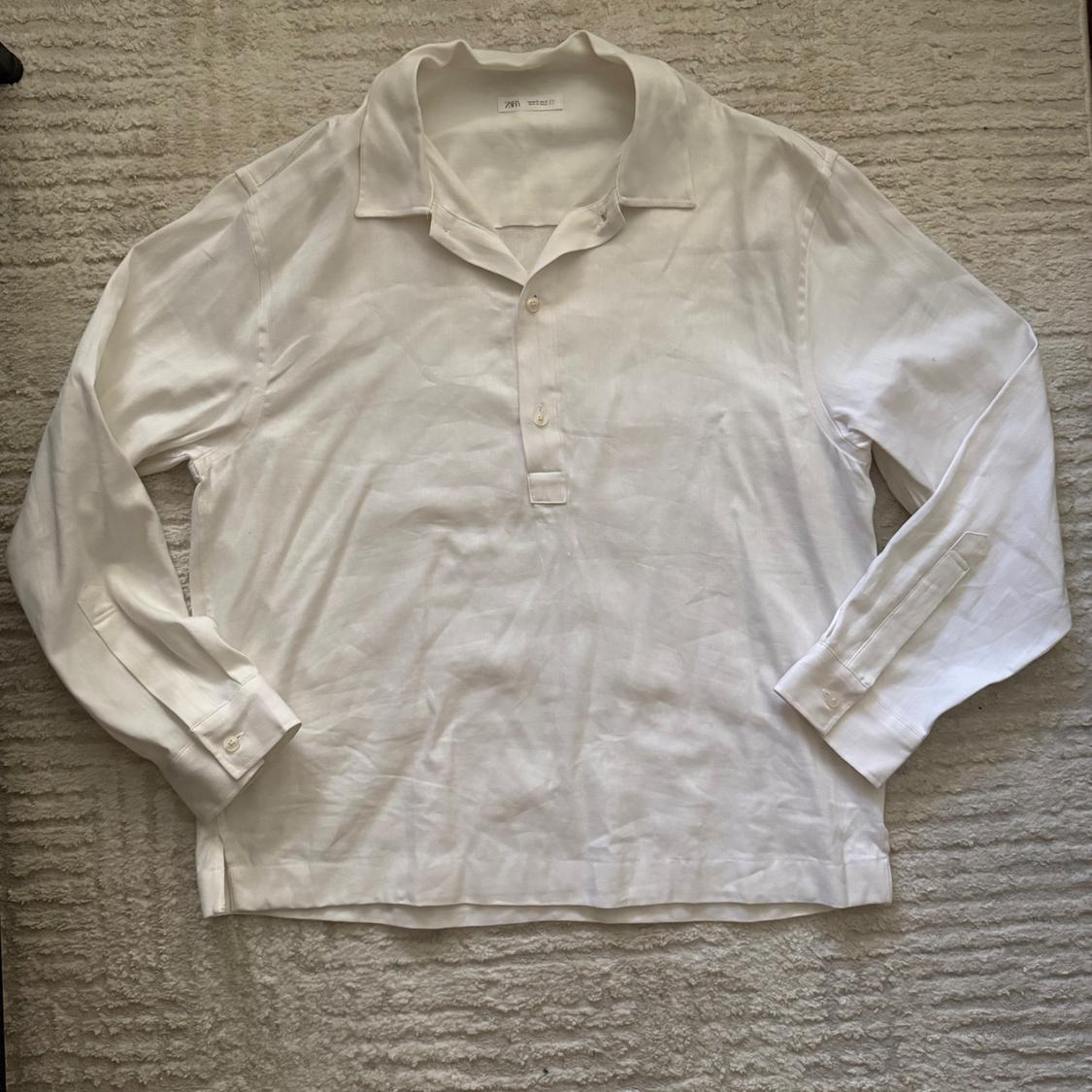 Long-sleeve white shirt with a polo collar, buttons, and a ZARA label, on a textured light-colored rug.