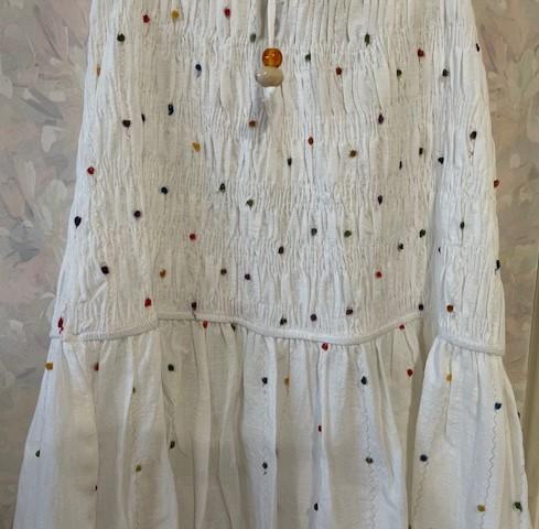 White dress with ruched texture and small coloured dots. Soft floral background in pastel shades.