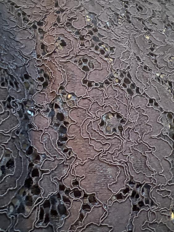Close-up of a black lace fabric with a floral design and shiny details on a dark background.