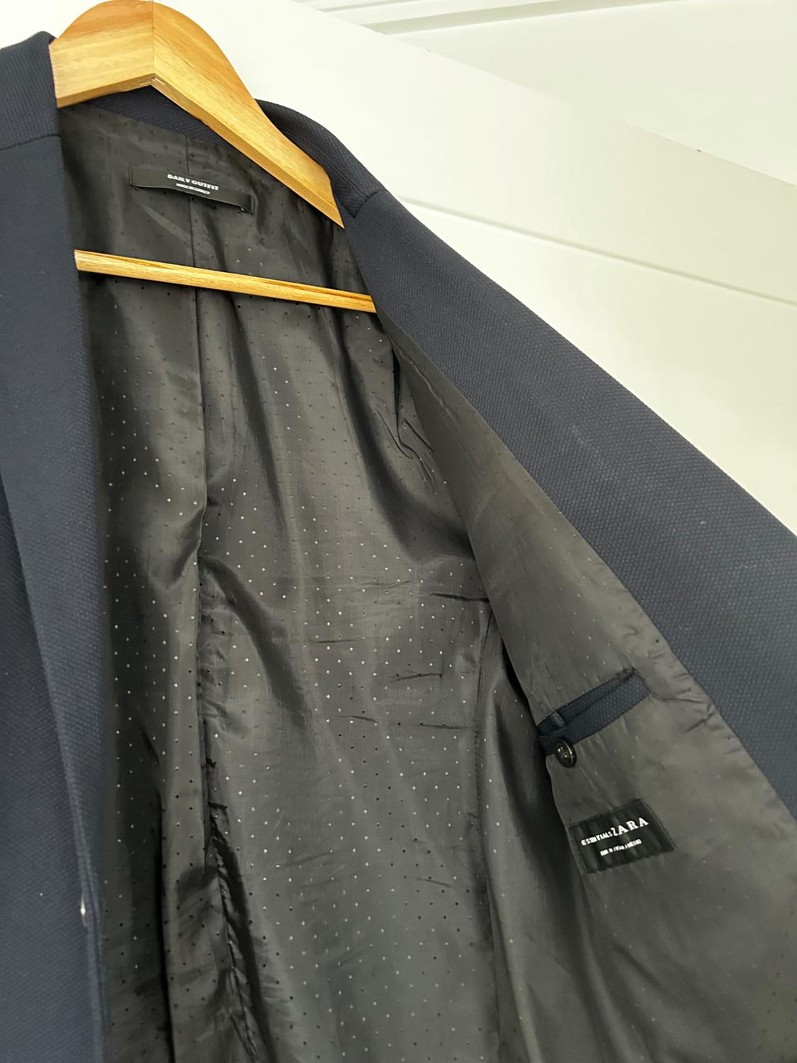 Navy blue jacket hanging on a wooden hanger, displaying the black inner lining with small white dots. Label visible.