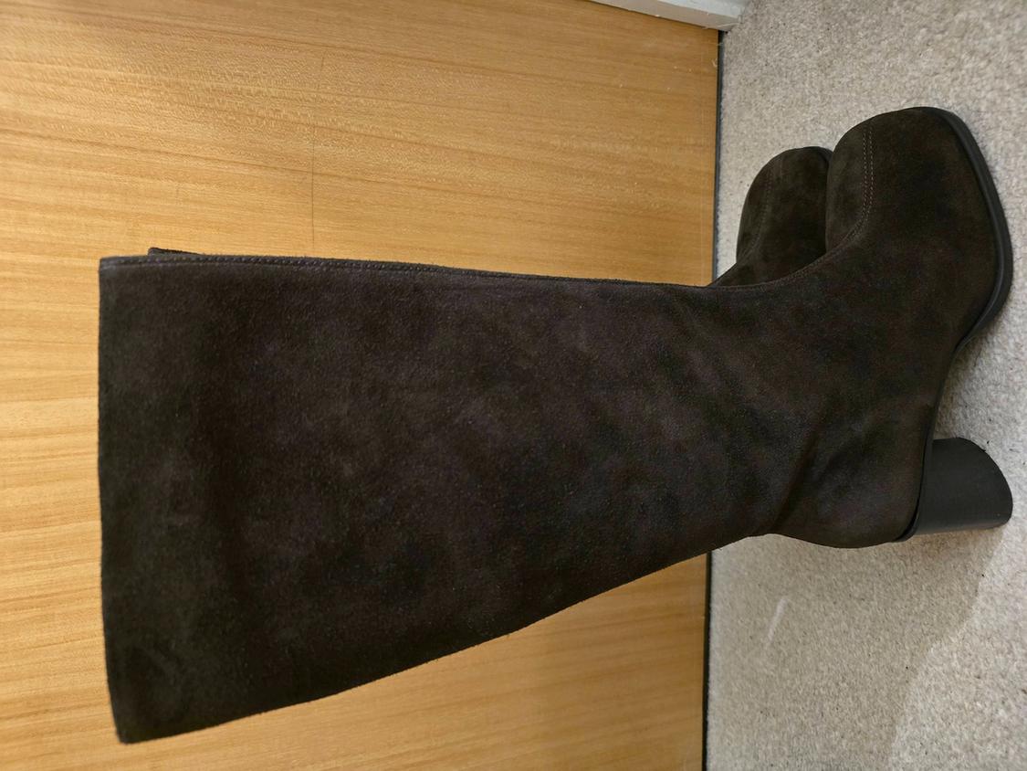 Dark brown suede knee-high boot with a block heel, resting on a wooden surface and beige carpet.