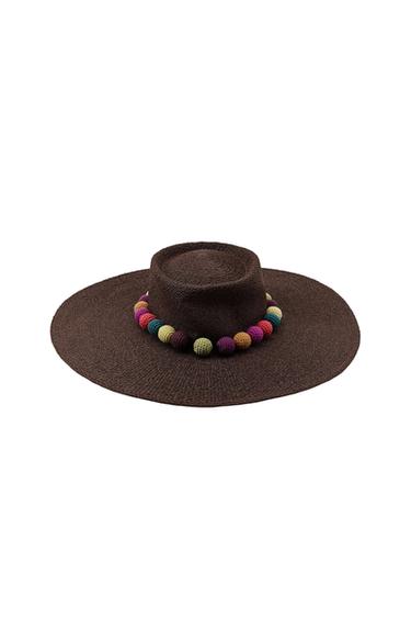 Dark brown woven wide-brimmed hat, decorated with coloured pom-poms at the base of the crown on a white background.