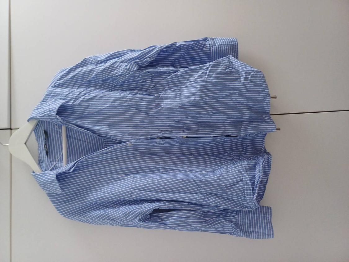 White-striped blue shirt hanging on a white hanger against a light background.
