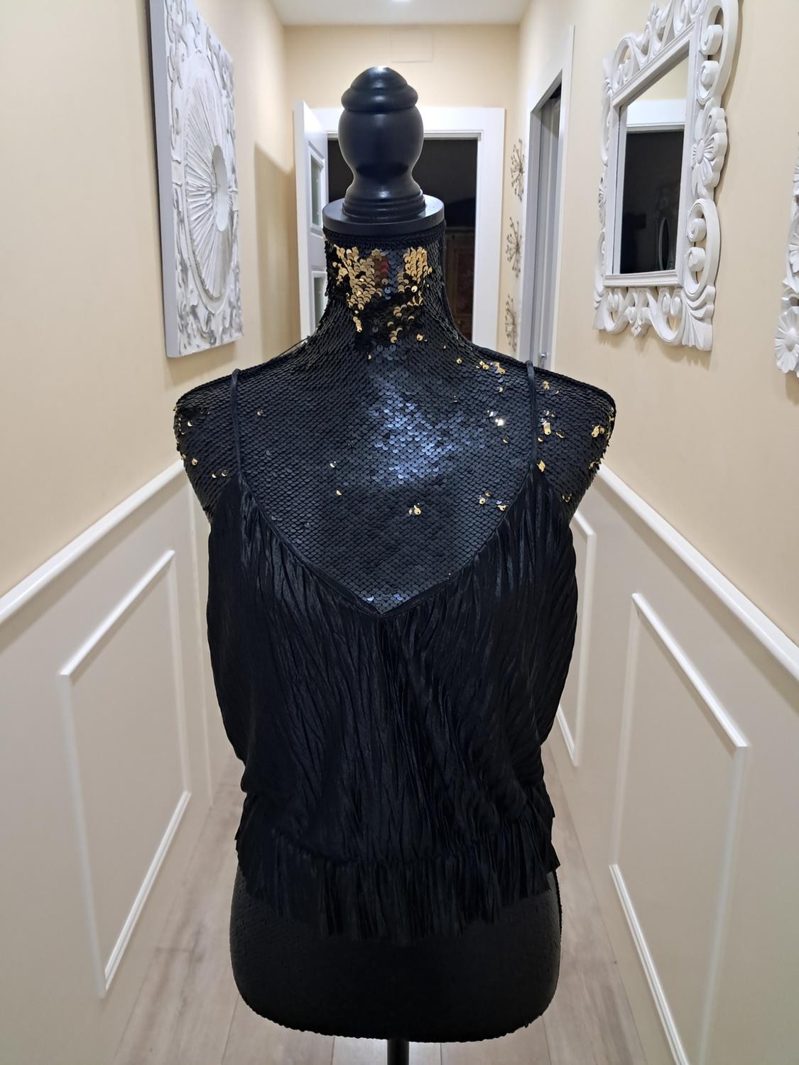Mannequin in a black pleated top with gold detailing in a hallway with light walls and decorative mirrors.