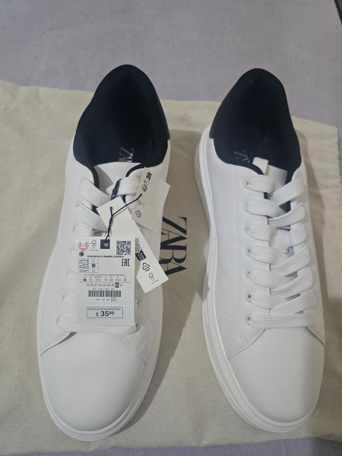 White trainers with a dark interior on a bag. Visible text: ZARA, 22 DEPORTIVO, 22 TRAINERS, 22 BASKETS, EAC, £35.99.