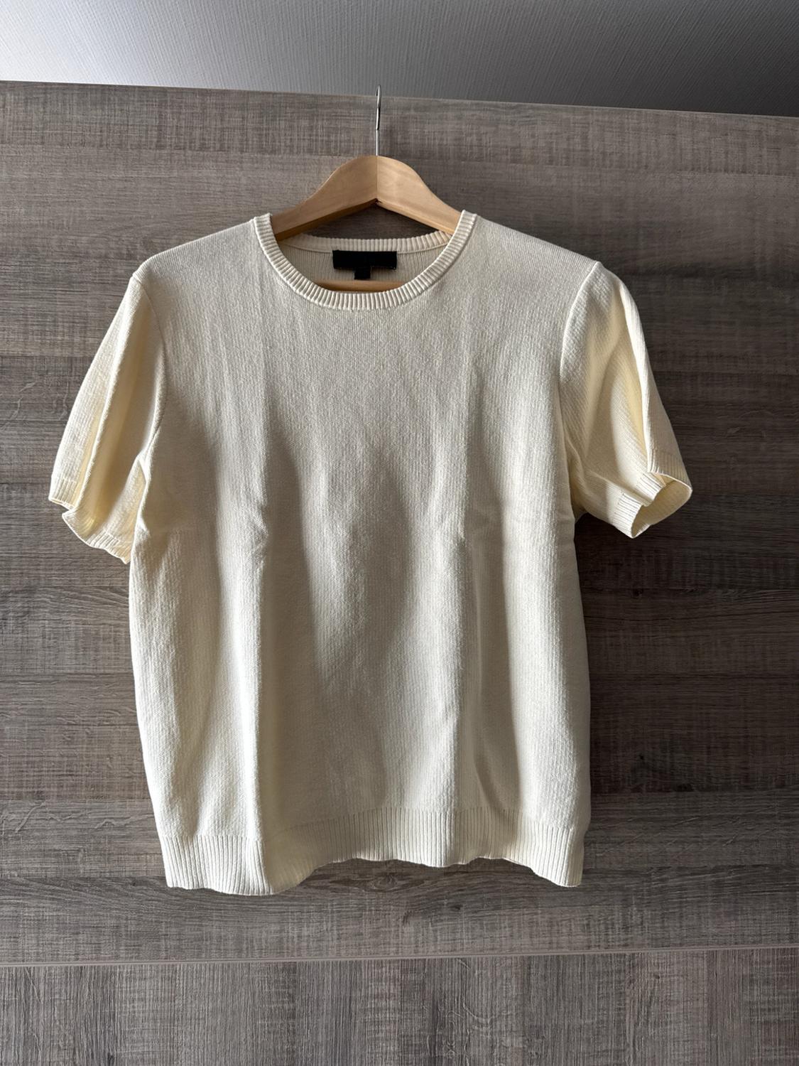Cream-coloured short-sleeved crew-neck knitted T-shirt, hanging on a hanger against a wooden background. Casual style.