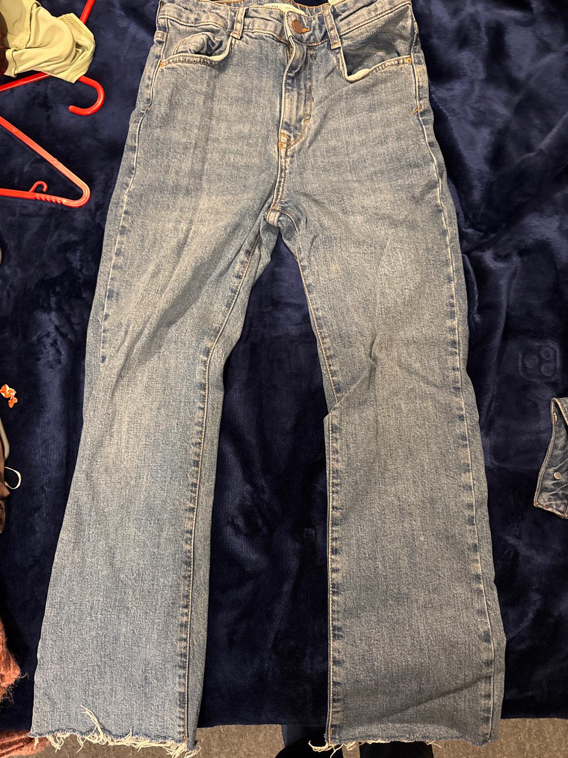 Worn blue jeans with a frayed hem over a dark blue blanket. Red hanger and clothes in the background.