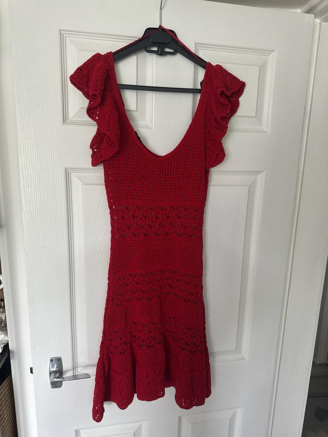 Red open-knit dress with ruffled sleeves and a V-neck,
hanging on a black hanger on a white door.