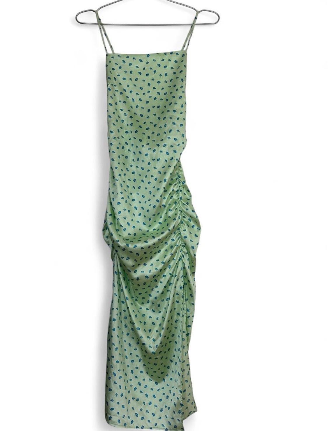 Light green dress with a blue floral print, thin straps, and gathered detail on the side, hanging on a hanger against a white background.