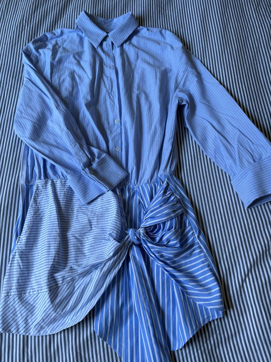 Blue and white striped shirt dress with a knotted detail at the waist, on a matching striped background.