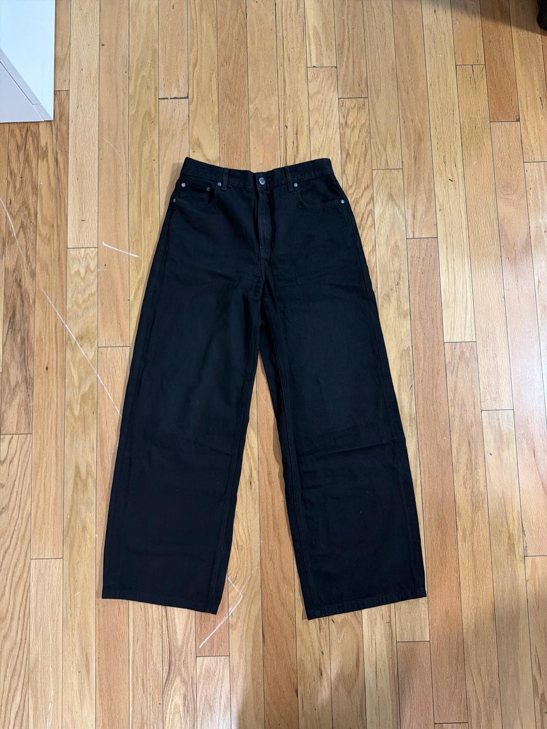 Black wide-leg jeans laid out on a light wood floor, casual style.