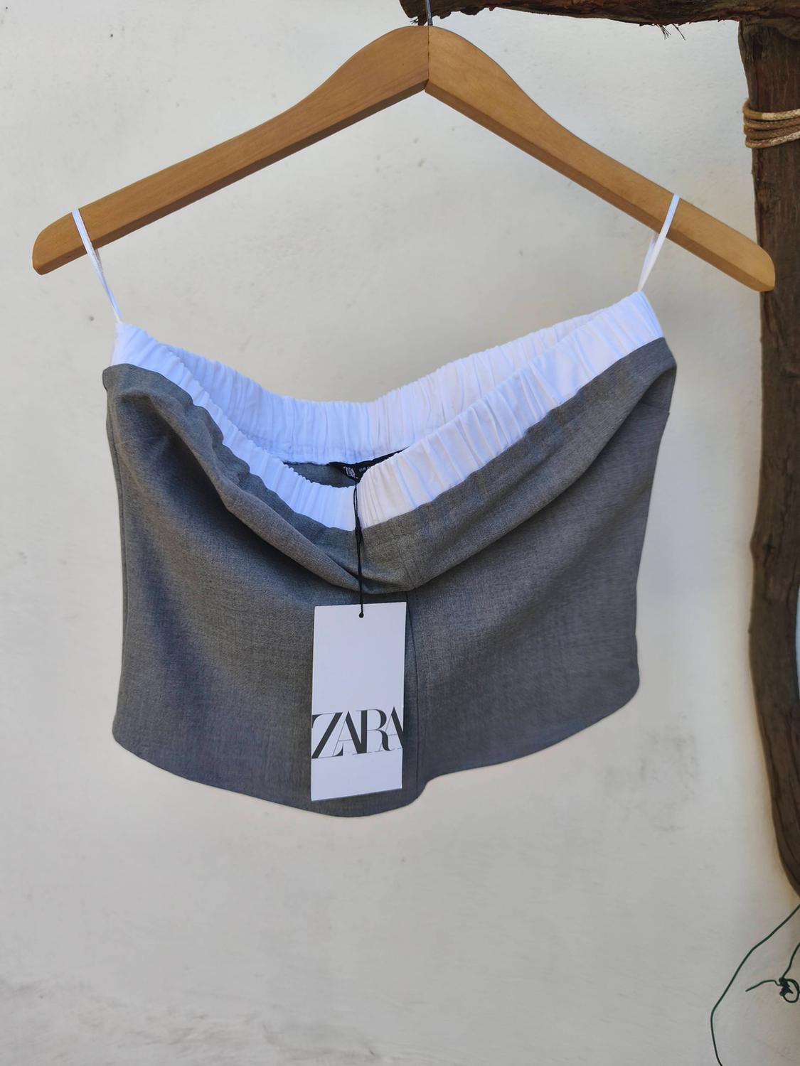 Grey and white top hanging on a wooden hanger with a Zara tag, white background and wooden branch on the right.