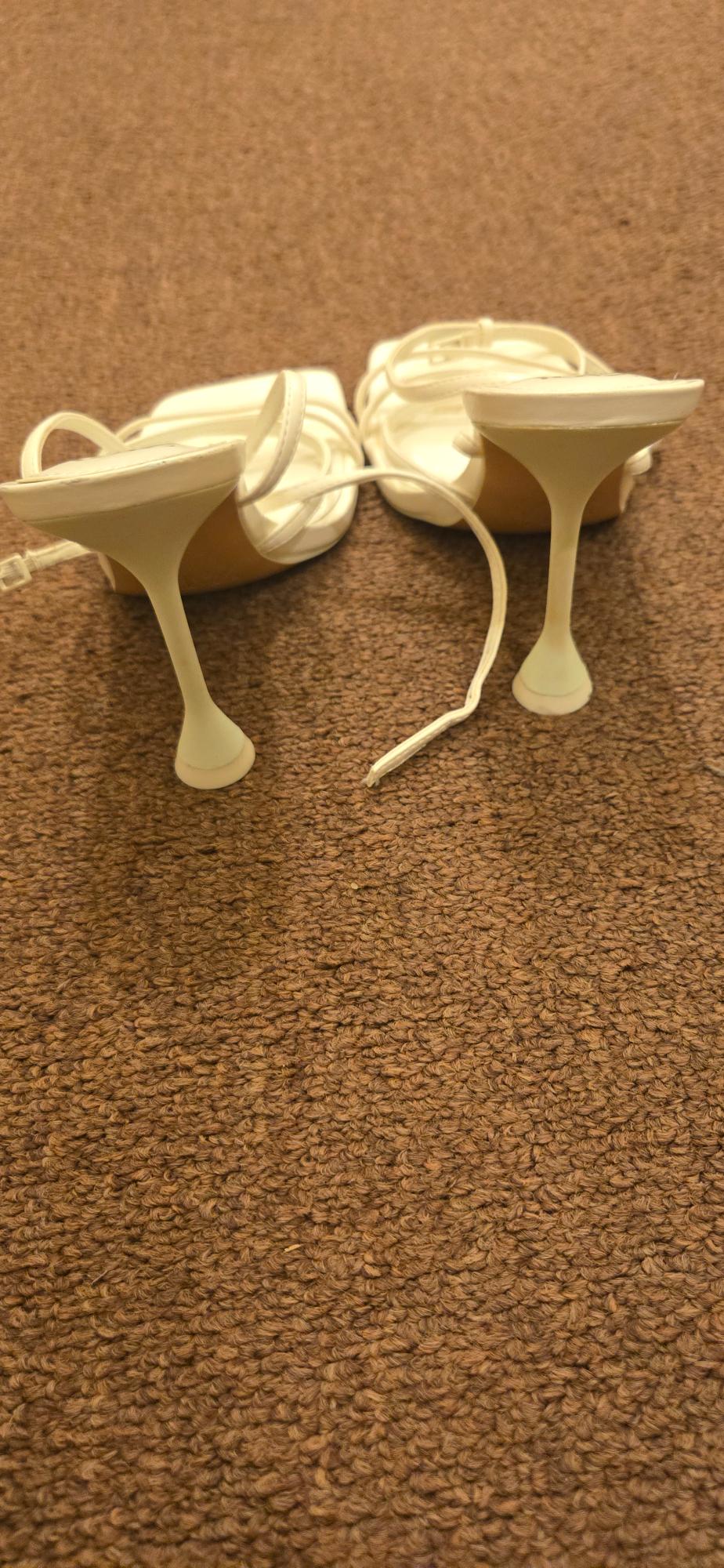 Rear view of white high-heeled sandals with thin straps on the floor.