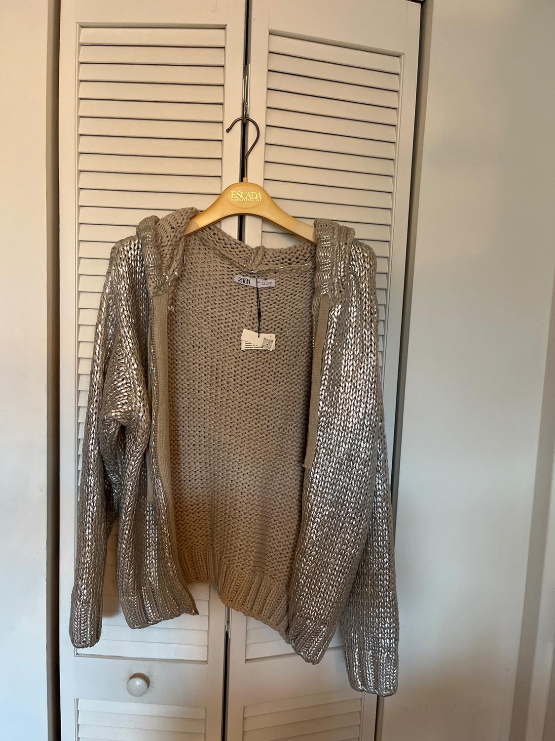 Beige knitted hoodie hanging on a wooden hanger with the brand "Escada", in front of a white wardrobe door.