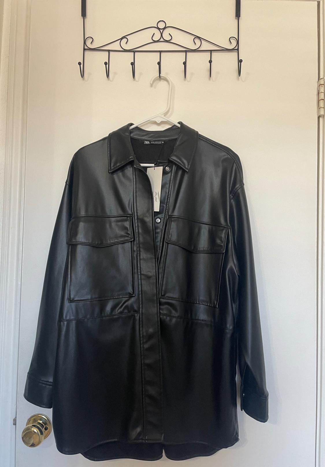 Black jacket hanging on a white hanger over a white door. The jacket has large pockets and a classic collar.