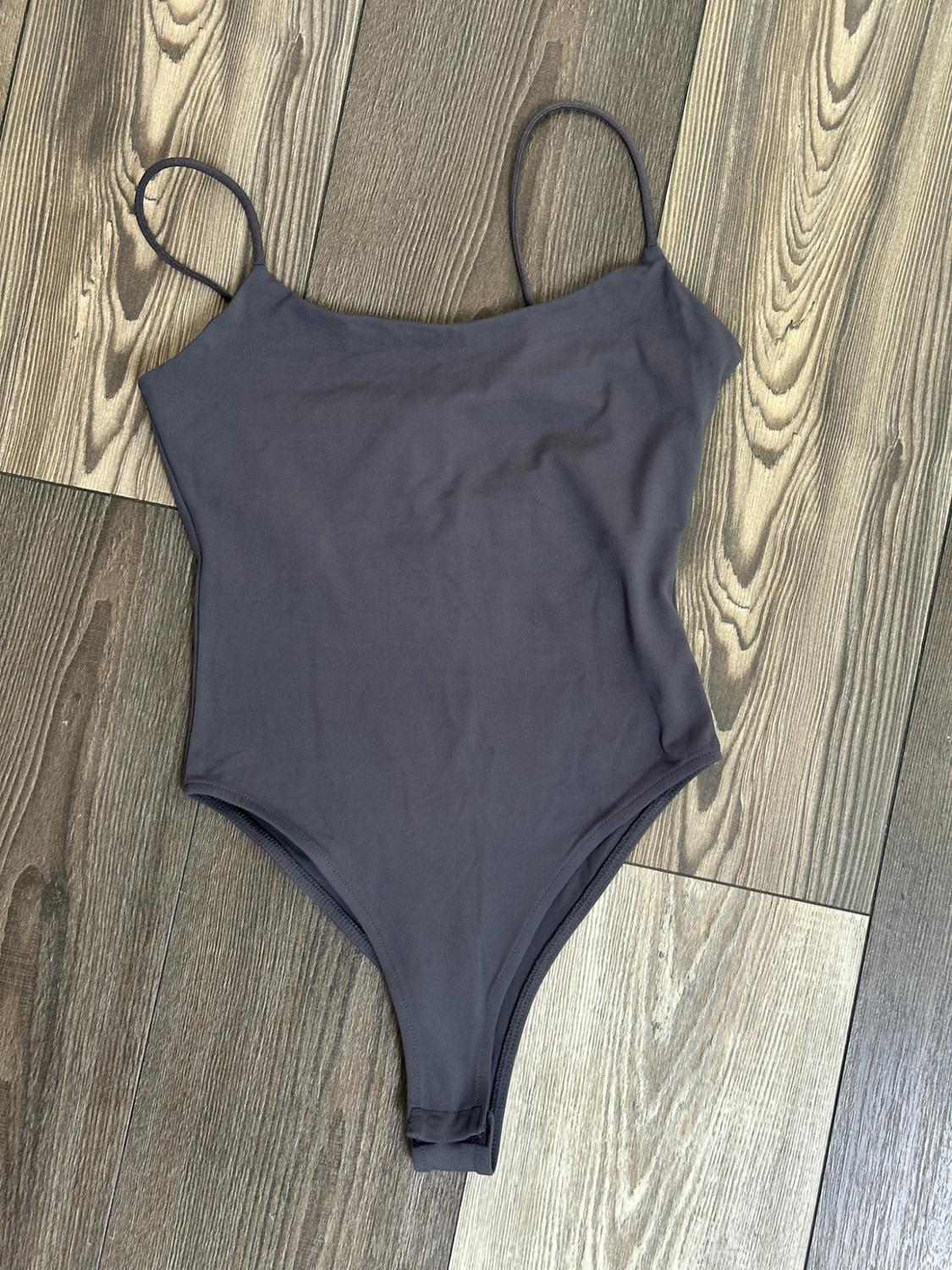 Dark grey bodysuit with thin straps on a wooden floor.