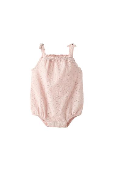 Pale pink baby romper with openwork embroidery, knotted straps, and a frill at the neckline, on a white background.