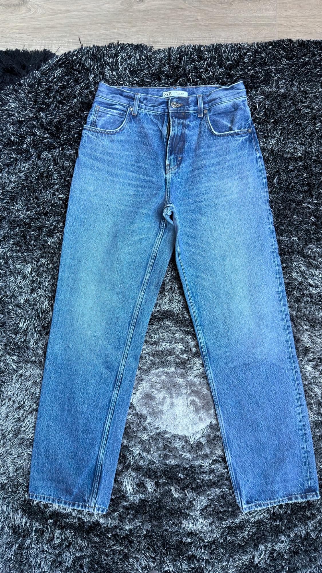 Τζιν παντελόνια μπλε χρώματος της μάρκας zara, απλωμένα πάνω σε έναν σκουρόχρωμο χαλί με μακριές τρίχες.
