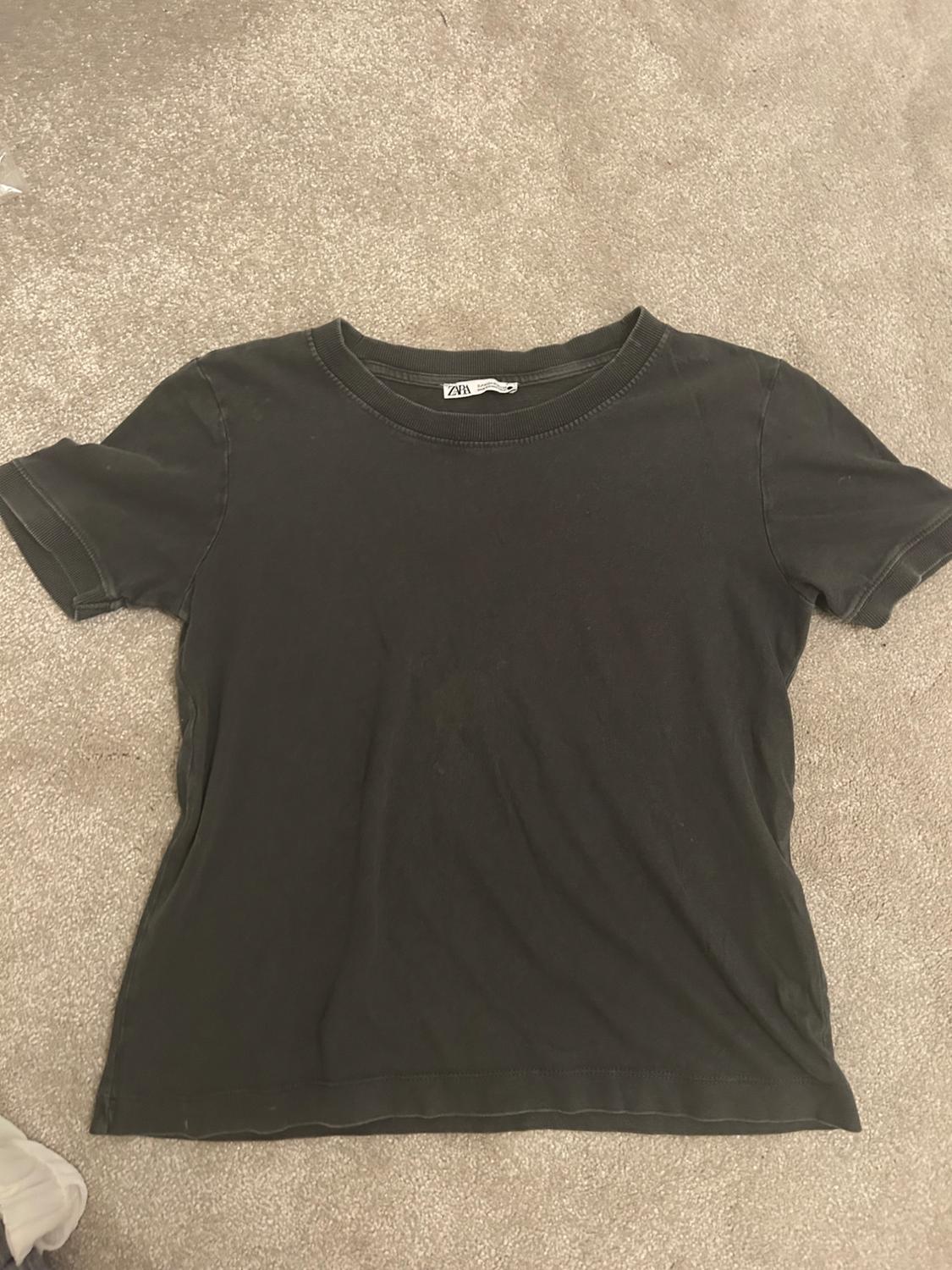 Black short-sleeved T-shirt on a beige carpet. Label visible on the neck with the text "ZARA".