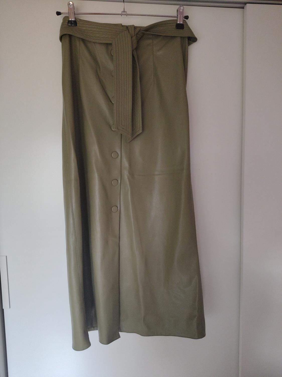 Olive green long skirt hanging on a hanger, with front buttons and a tie belt at the waist. White background.