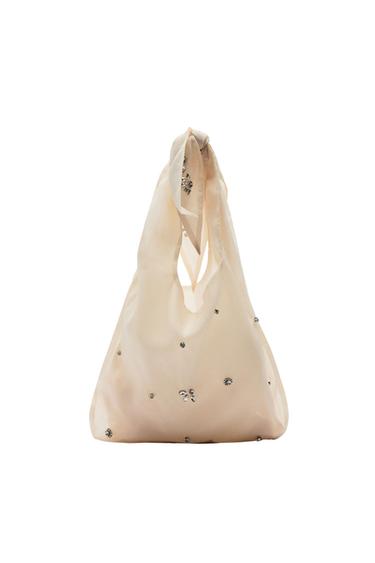 Beige semi-transparent fabric bag with shiny embellishments and a knotted handle on a white background.