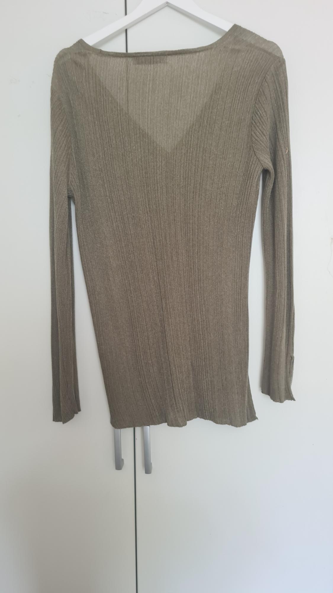 Fine-knit beige jumper with long sleeves, hanging on a white coat hanger in front of a white wardrobe.