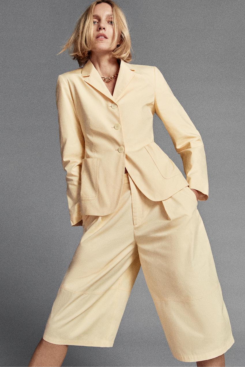 Conjunto de chaqueta amarilla con cuello solapa, tres botones y bolsillos frontales de parche, y pantalón ancho corto a juego.