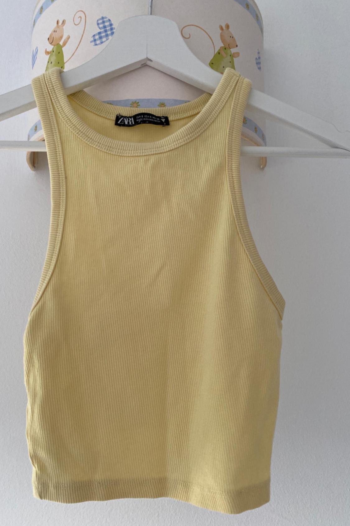 Front view of a yellow sleeveless round-neck top on a white hanger.